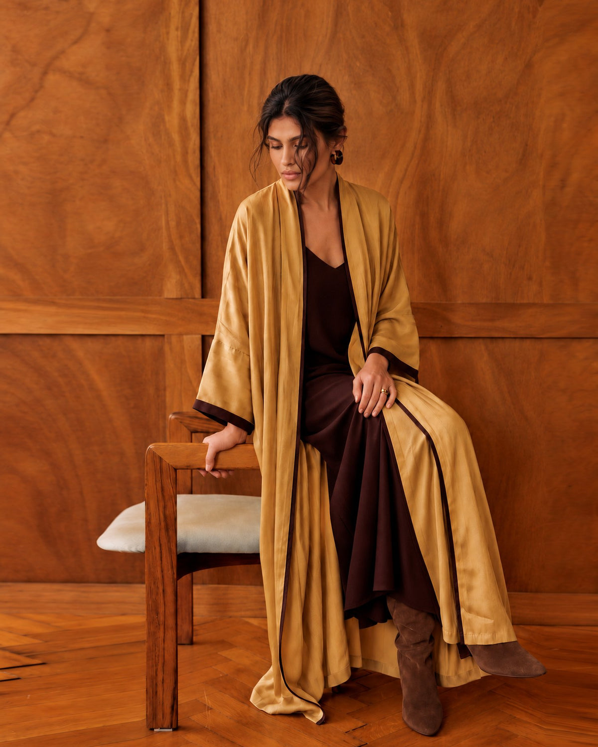 Model in a goldenrod washed-silk abaya over a dark brown dress, seated in a wood-panelled room