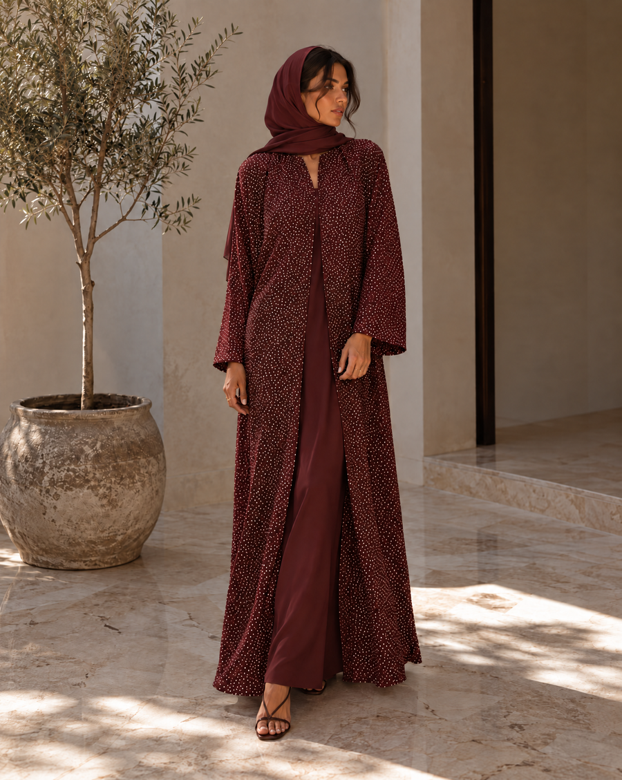 Burgundy embellished abaya with matching headscarf in a stone courtyard