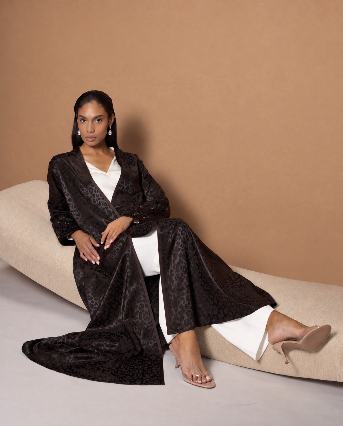 Model in the CODE-0425 tan viscose abaya coat with cream piping, glasses and brown gloves, in a wood-panelled elevator