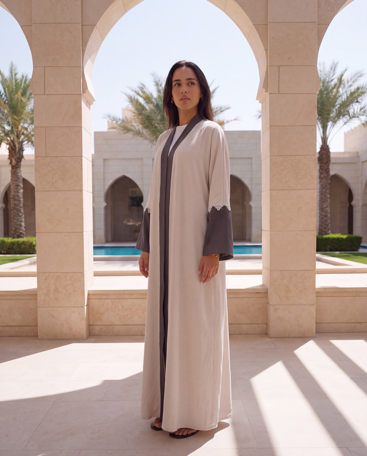 Chika beige crepe abaya with grey trim and sleeves under stone arches