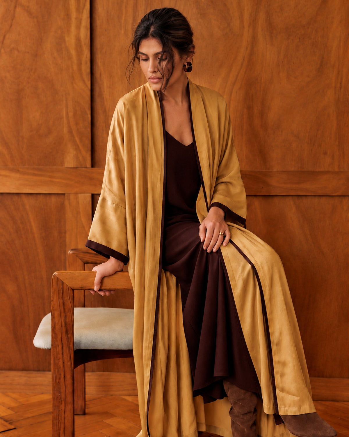 Model in a goldenrod washed-silk abaya over a dark brown dress, seated in a wood-panelled room