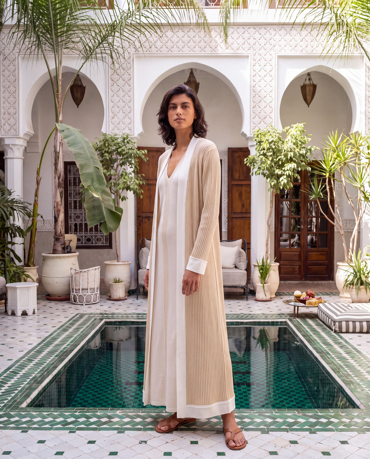Model in the Shabaka Jameela ivory silk abaya set beside a tiled courtyard pool