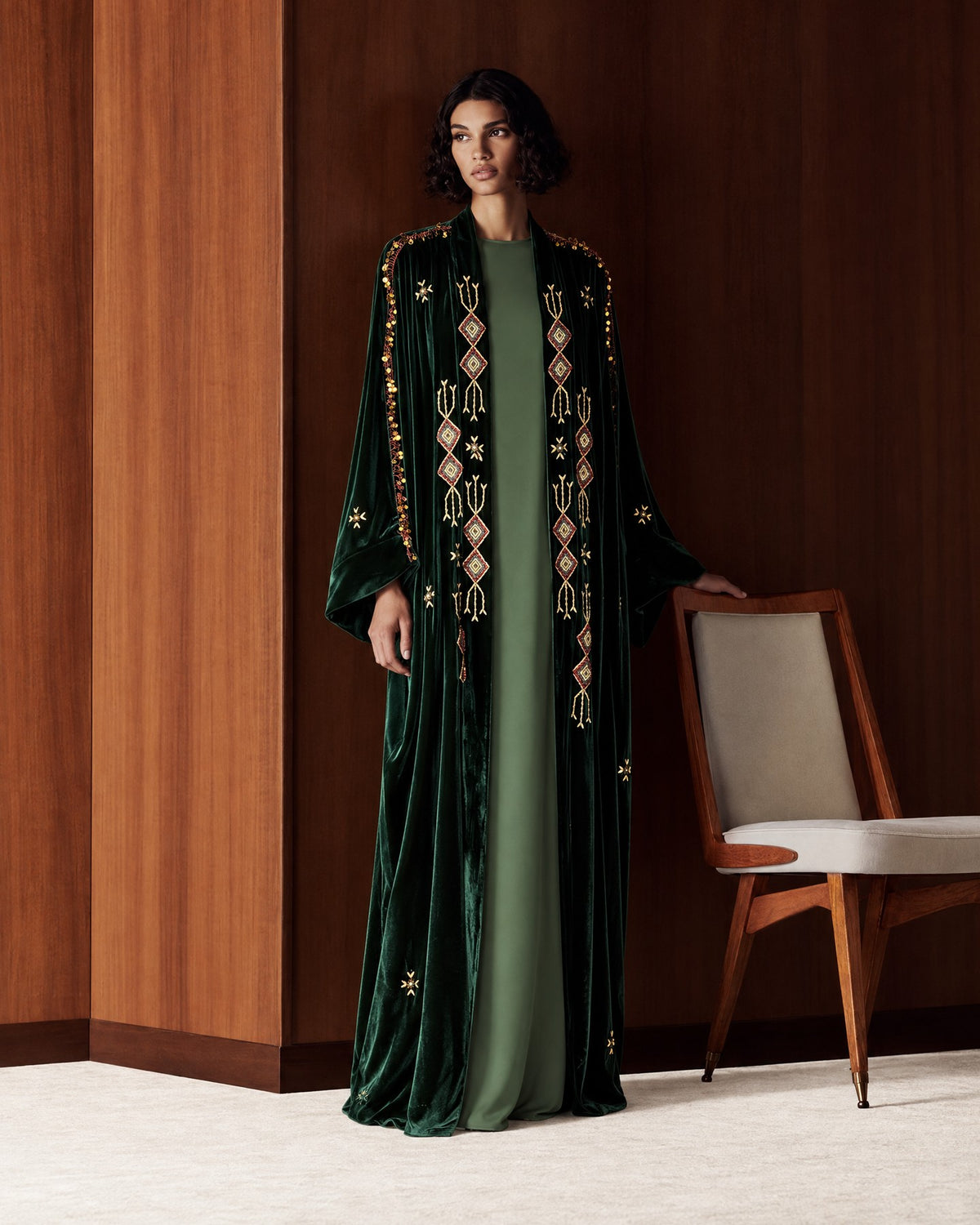 Two autumn looks in wood-panelled rooms: a dark green velvet abaya with gold geometric embroidery over a green dress, and a goldenrod washed-silk abaya over a dark brown dress