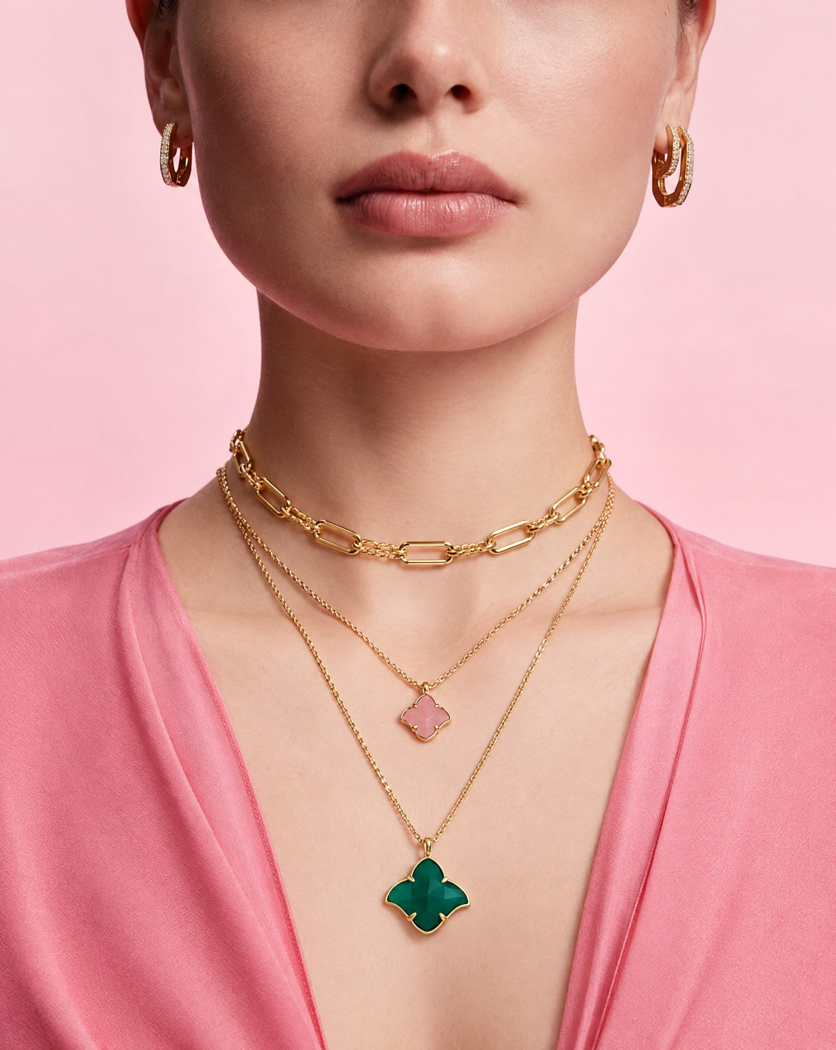 Three layered gold necklaces: a link chain, a pink clover pendant and a green clover pendant