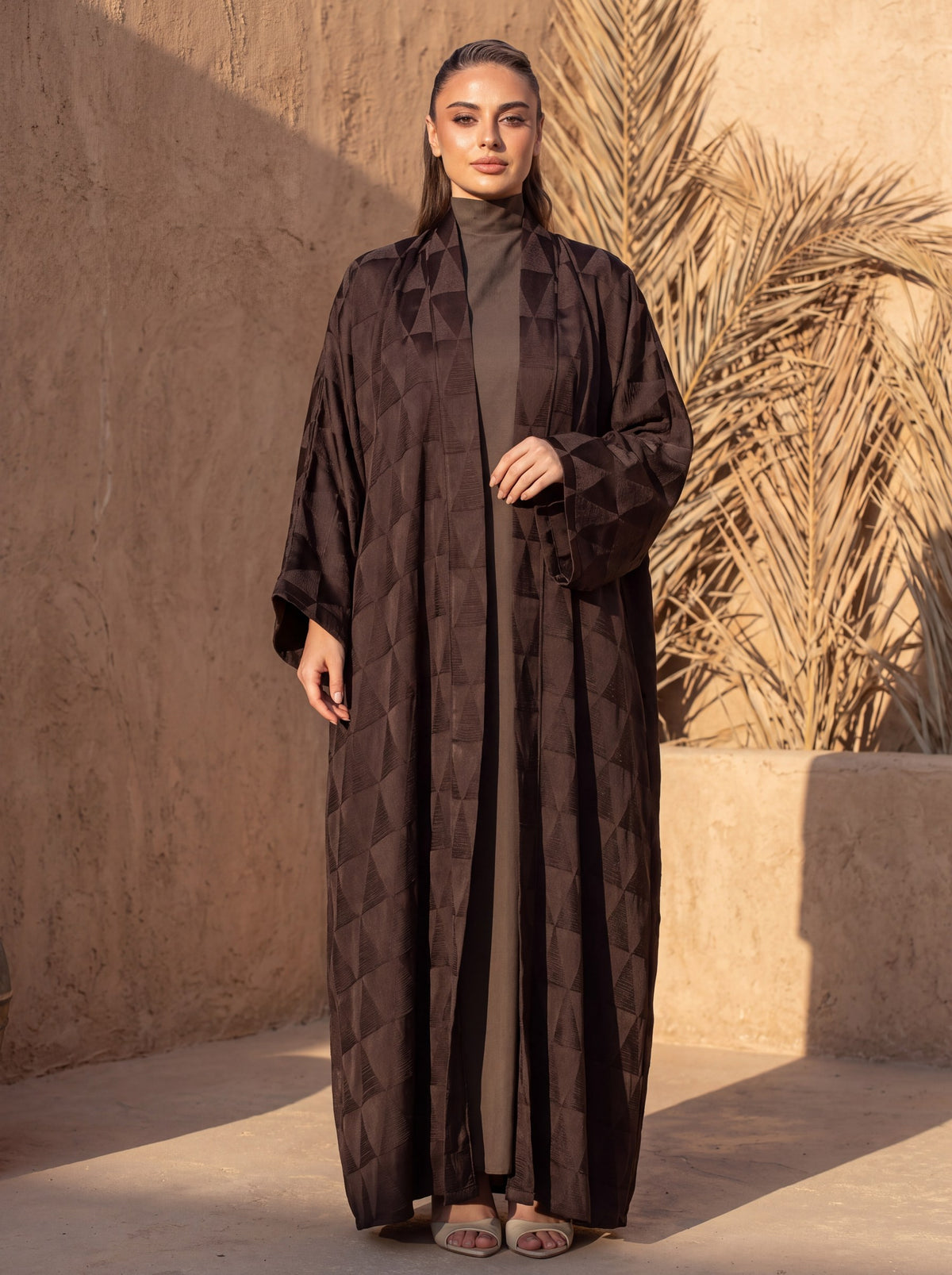 Brown jacquard abaya in an earthen courtyard