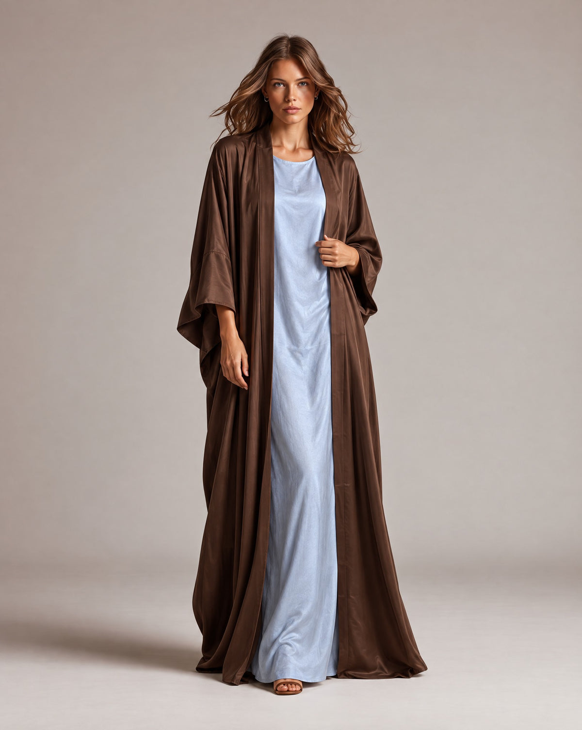Model in a chocolate brown Japanese silk abaya worn open over a pale blue dress, in a studio