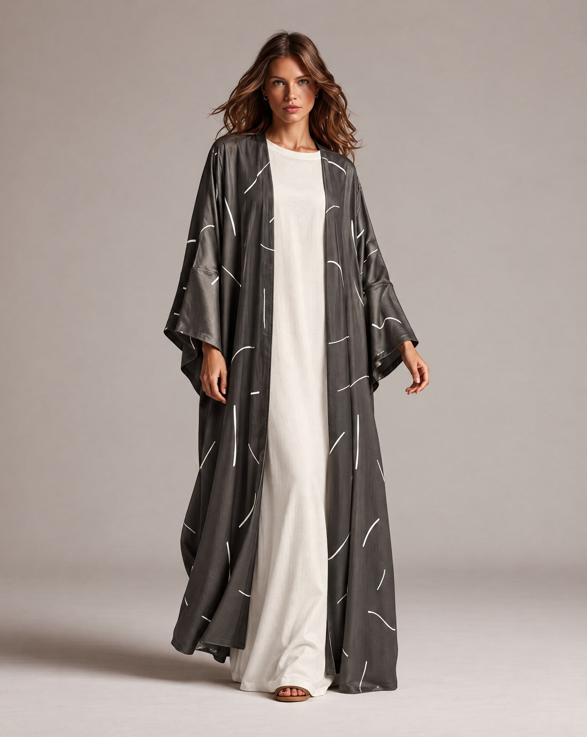 Model in a charcoal grey Japanese silk abaya with a white line print, worn open over an ivory dress