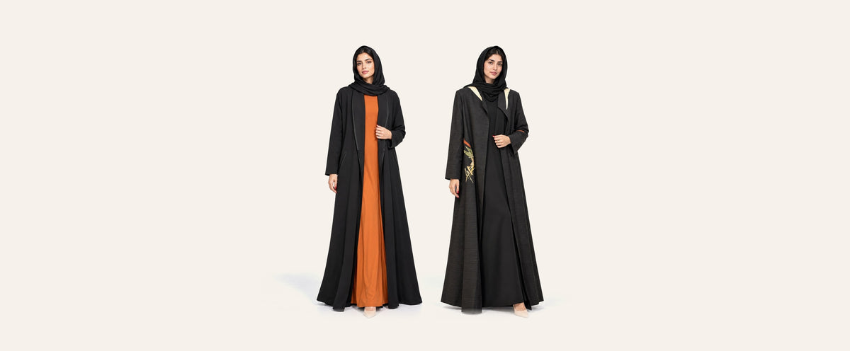 Amber Feroz AF Coat black crepe abaya over an amber dress, beside the SNM black jacquard abaya
