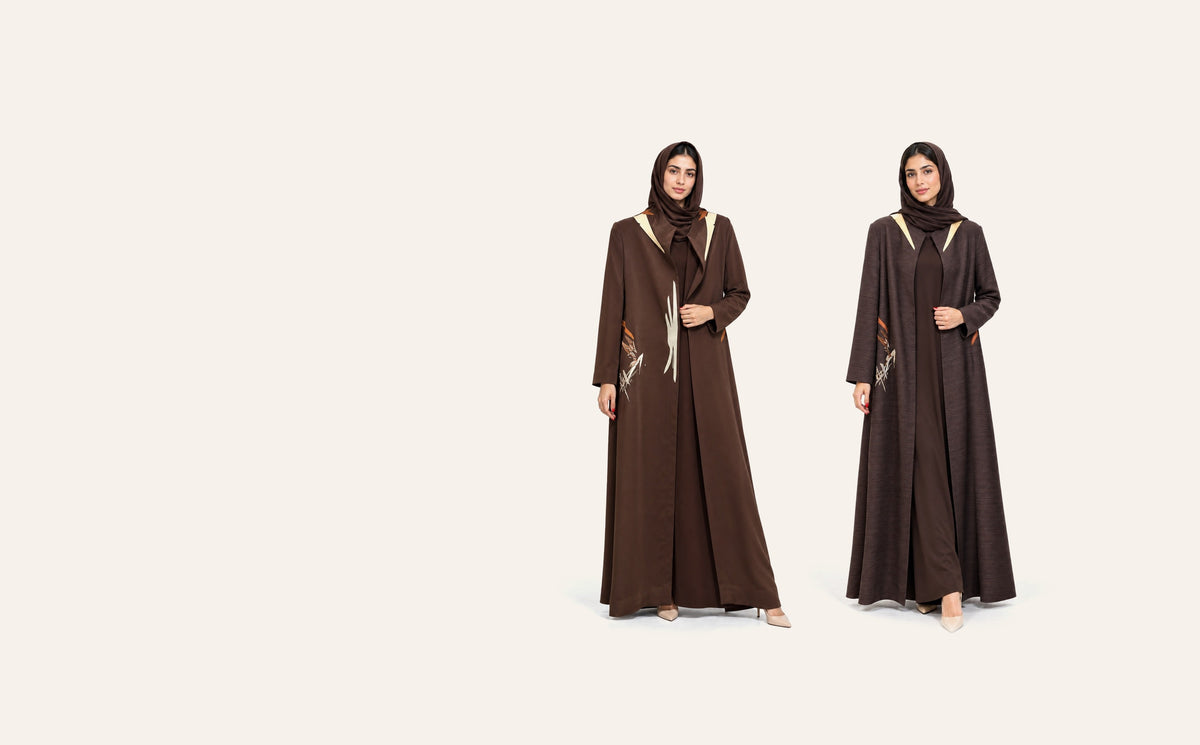 Amber Feroz SNM brown crepe abaya beside the SNM plum jacquard abaya, on a plain cream studio background