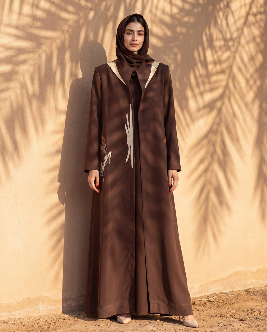 Brown crepe abaya with a hand-painted panel against a sandstone wall
