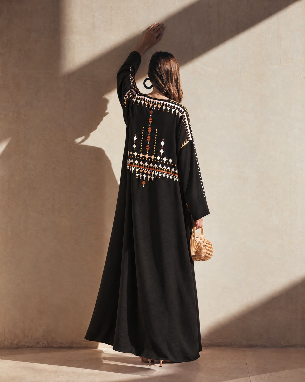 Model in a black abaya with an embroidered back, in afternoon shadow