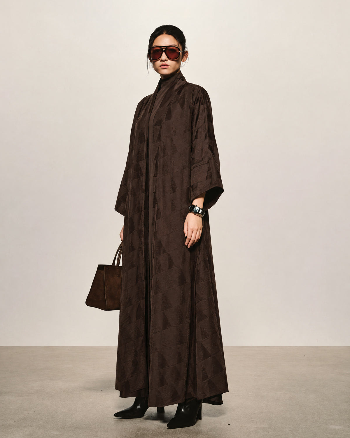 Model in a dark brown jacquard abaya with sunglasses and a leather tote
