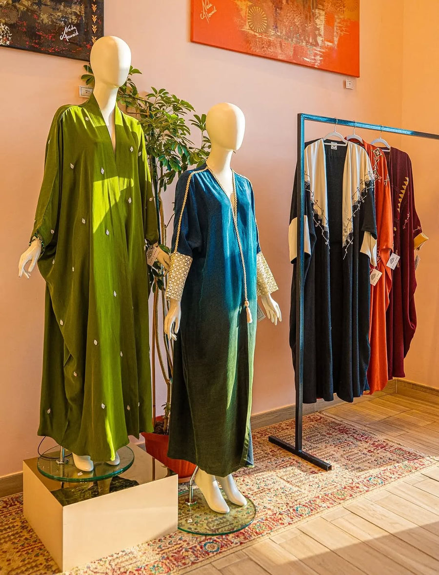 Green and teal embroidered abayas on mannequins beside a rail of embroidered abayas